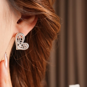 Detailed close-up of a silver hollow-woven heart earring with crystals on a model's ear