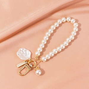 Close-up of pearl bead keychain with white shell charm and handmade metal tag on pink silk