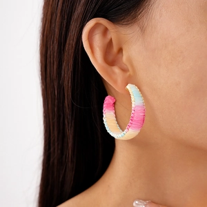 Close-up of rainbow woven raffia C-shape hoop earrings worn by a female model