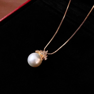 Close-up of elegant gold box chain necklace with white pearl pendant and zircon accents