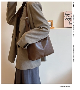 Sac à bandoulière en cuir marron foncé porté par un mannequin dans un intérieur minimaliste