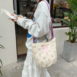 Détail d'un sac seau matelassé à fleurs avec bandoulière violette et écusson rose
