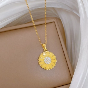 Close-up of golden sunflower pendant with yellow enamel inlay on a beige jewelry box