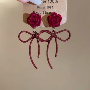 Elegant burgundy velvet rose earrings with bow tassel design on a display card