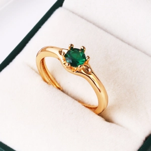 Detailed view of a gold-plated ring with a round-cut emerald green gemstone in a jewelry box