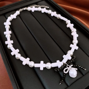 Macro detail of white matte cross beads and bow pendant on retro pearl necklace