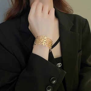 Detailed macro view of wide golden cutout cuff bracelet with intricate floral pattern