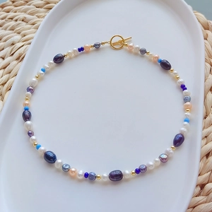 Multicolor natural freshwater pearl necklace with golden toggle clasp on a white tray