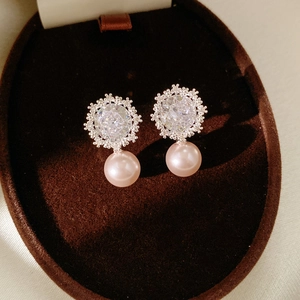 Macro shot of pink pearl earrings with shimmering zircon crystals on dark velvet tray