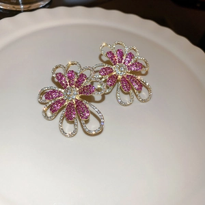 Detail von Goldohrringen in Blumenform mit rosa Strasssteinen und funkelnden Kristallen