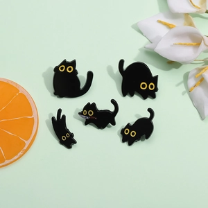 Set of five cute black cat enamel pins with yellow eyes on a fresh green background