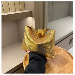 Détail montrant une main tenant un sac à main à paillettes dorées sous une lumière vive