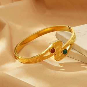 Detailed close-up of gold evil eye bangle with red and green gems on marble and silk