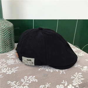 Vintage black cotton newsboy cap with side fashion label on a white lace tablecloth