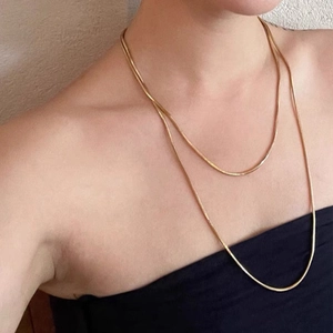 Detail of layered gold snake bone chain necklace worn by a model in soft light