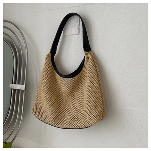 Detail of the woven mesh texture and smooth black shoulder strap of the straw beach bag