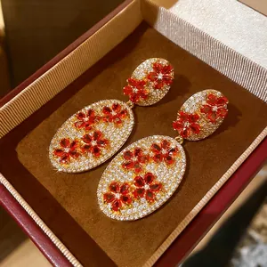 Vintage gold oval drop earrings with zircon floral pattern and red gems in a box