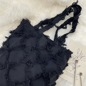 Close-up of black fringe tassel tote bag with macro textured plaid on soft white faux fur