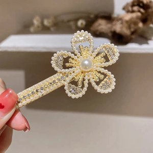 Detail of a gold flower hair clip featuring inlaid pearls and sparkling rhinestones