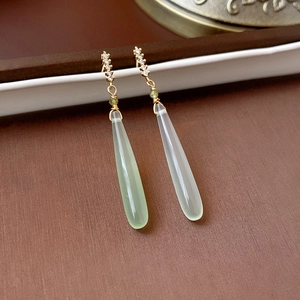 Macro view of long waterdrop earrings with gold bars and pale green jade-like pendants