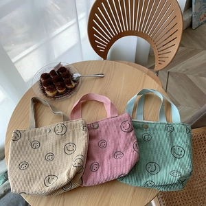 Close-up of corduroy tote bags in beige pink and green with a smiling face print
