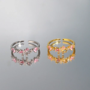 Macro shot of gold and silver bow rings with pink heart zircons on a reflective surface