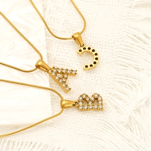 Golden stainless steel necklace with crystal-paved initial pendants on white marble