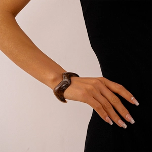 Close-up of wavy irregular resin bangle with dark brown marble texture on model wrist