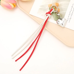 Red and white heart-shaped braided leather keychain with tassels on a pink plate