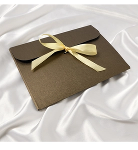 Detail of dark brown envelope gift box with a light yellow ribbon bow on white silk