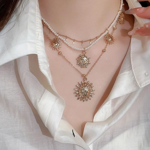 Detail of layered gold sun pendant necklace with pearls on a model wearing a white shirt