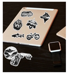 Black and white gothic stickers with nature silhouettes on a tablet and wooden desk