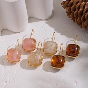 Gros plan de boucles d'oreilles carrées en résine rose beige et marron dorées