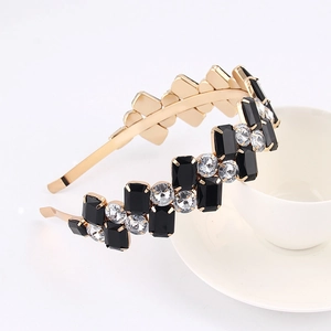 Detailed close-up of golden metal headband with black and clear rhinestones on white background