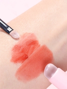 Macro view of silicone lip brush and fiber brush applying orange lip glaze on skin