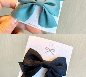 Close-up of dark green and black ribbed fabric hair clips on branded display cards