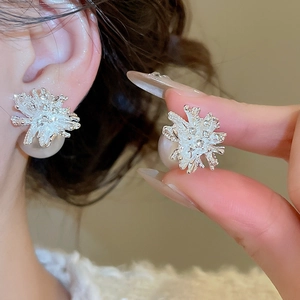Close-up of floral silver earrings featuring textured petals and large pearl backings