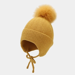 Détail du bonnet en tricot jaune avec cache-oreilles, pompon en fausse fourrure et lanières
