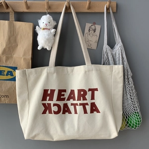 Detail of off-white canvas tote with red Heart Attack print hanging on a wooden hook