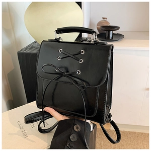 Detail of black glossy mini backpack featuring criss-cross straps and long tassel bow