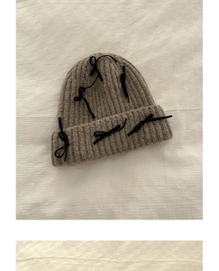 Detailed knit texture of tan wool beanie with decorative black satin bows