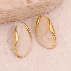 Macro detail of irregular geometric gold earrings with creamy white marble texture