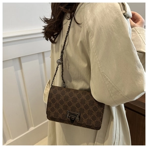 Detail of a brown vintage print crossbody bag with a metal chain and gold ball accent