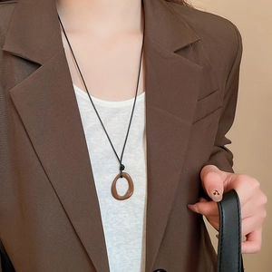 Détail d'un pendentif ovale irrégulier en résine brune sur un long collier cordon noir