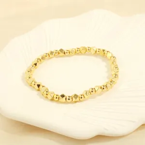 Detailed shot of golden beaded bracelet with geometric charms on a white ceramic tray