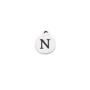 Macro detail of a round stainless steel charm featuring an engraved capital letter N