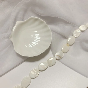Macro view of polished white mother of pearl oval beads in a shell ceramic dish