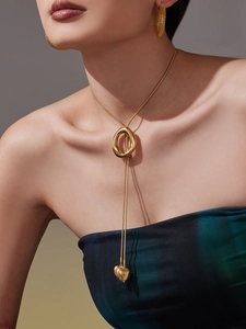 Close-up of golden lariat heart necklace and textured earrings on a model neck