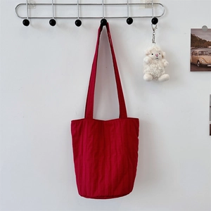 Primer plano del bolso tote acolchado rojo en nailon con costuras verticales en la pared