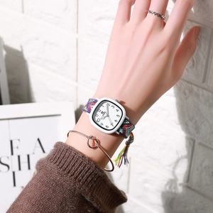 Detail of square quartz watch with colorful woven strap and gold knotted bracelet